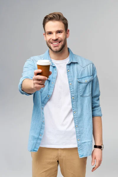 Retrato de jovem caucasiano bonito em camisa jeans sobre fundo claro segurando xícara de café para ir — Fotografia de Stock