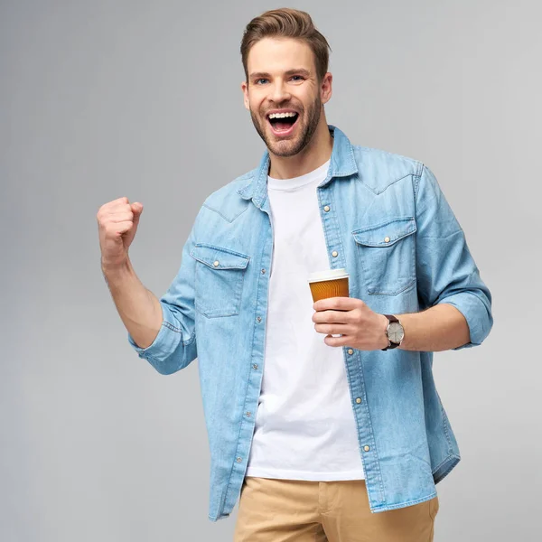 Retrato de jovem caucasiano bonito em camisa jeans sobre fundo claro segurando xícara de café para ir — Fotografia de Stock