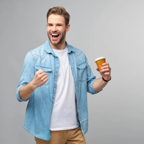 Portret van jonge knappe blanke man in jeans shirt over lichte achtergrond met kopje koffie te gaan — Stockfoto