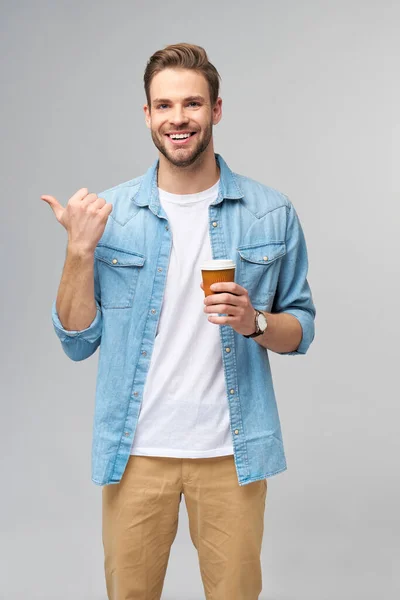 Portrait de jeune homme caucasien beau en jeans chemise sur fond clair tenant tasse de café à emporter — Photo