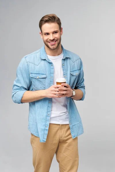 Porträtt av ung vacker kaukasisk man i jeans skjorta över ljus bakgrund innehav kopp kaffe att gå — Stockfoto