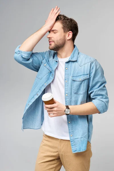 Retrato de joven guapo hombre caucásico en jeans camisa sobre fondo claro sosteniendo taza de café para llevar —  Fotos de Stock