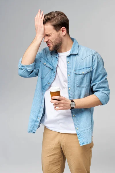 Retrato de joven guapo hombre caucásico en jeans camisa sobre fondo claro sosteniendo taza de café para llevar —  Fotos de Stock