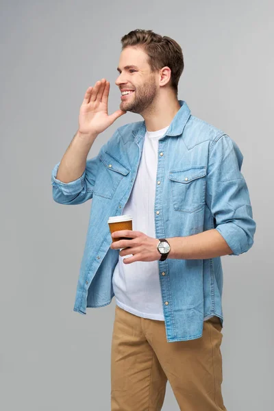 Portrait de jeune homme caucasien beau en jeans chemise sur fond clair tenant tasse de café à emporter — Photo