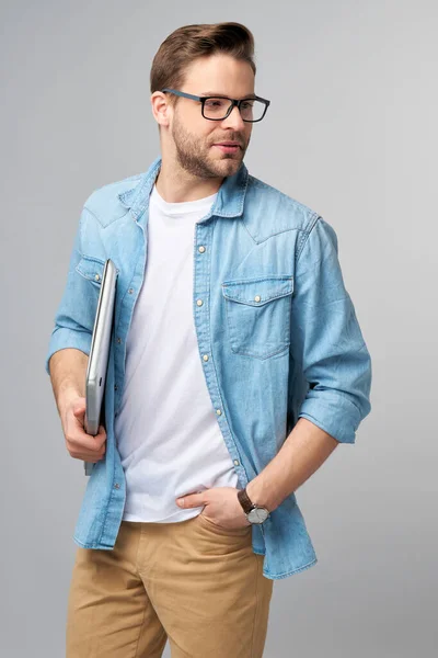 Jeune homme barbu concentré portant des lunettes habillé en jeans chemise tenant ordinateur portable isolé sur fond de studio gris — Photo