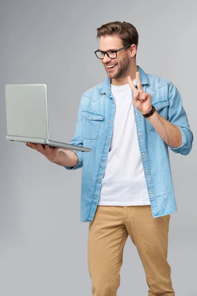 Kotlu gömlek giymiş, gözlüklü, sakallı bir genç adam elinde dizüstü bilgisayarla gri stüdyo arka planında izole edilmiş. — Stok fotoğraf