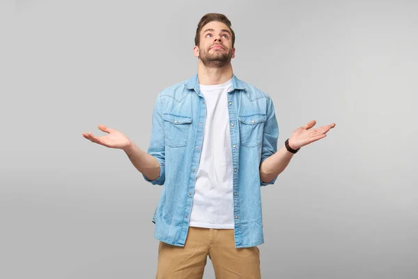 Retrato de un joven confuso y despistado con camisa vaquera de pie sobre fondo gris —  Fotos de Stock