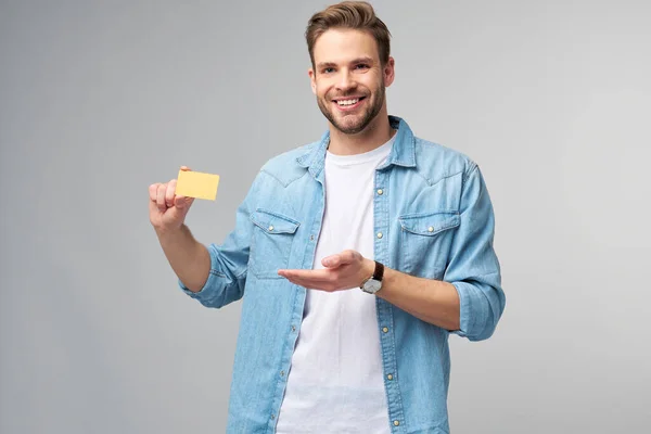 Guapo feliz joven mostrando en blanco banco cor tarjeta de descuento —  Fotos de Stock