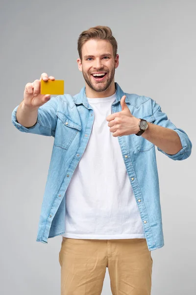 Guapo feliz joven mostrando en blanco banco cor tarjeta de descuento — Foto de Stock