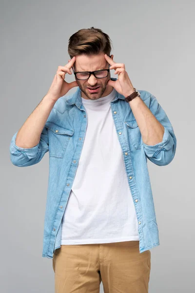 Frustrado joven caucásico hombre en jeans camisa tocando la cabeza con la mano mientras está de pie sobre fondo gris estudio —  Fotos de Stock