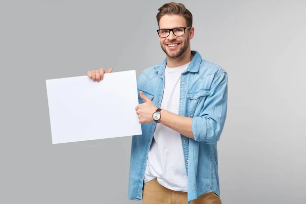 Retrato de un joven guapo feliz sosteniendo tarjeta blanca en blanco o signo sobre fondo blanco —  Fotos de Stock