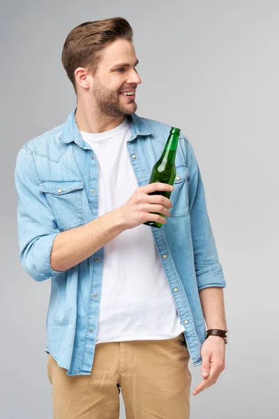 Ung man med jeans skjorta Flaska öl står över Grå bakgrund — Stockfoto