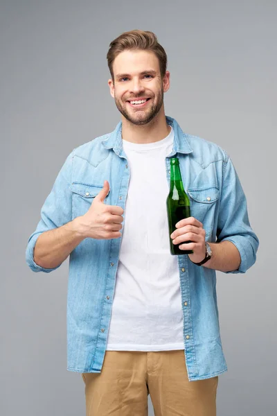 Молодий чоловік тримає в джинсах сорочку пива, що стоїть над сірим фоном. — стокове фото