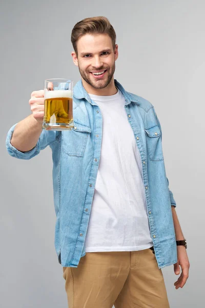 Jeune homme tenant un jeans chemise tenant un verre de bière debout sur fond gris — Photo