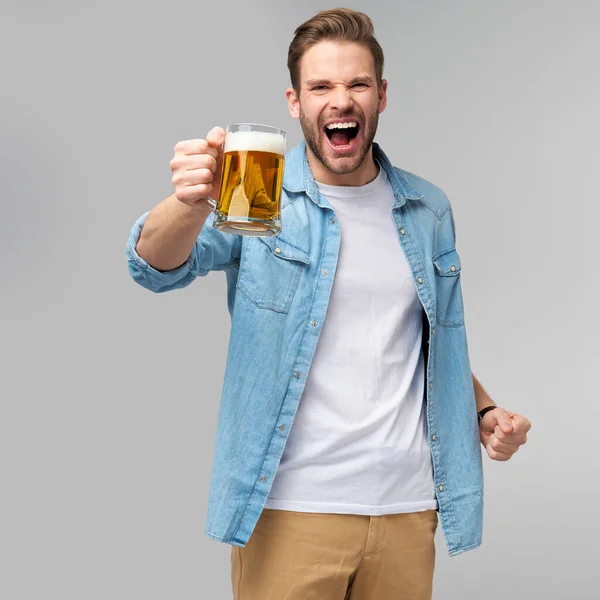 Homem jovem segurando vestindo camisa jeans segurando vidro de cerveja em pé sobre fundo cinza — Fotografia de Stock