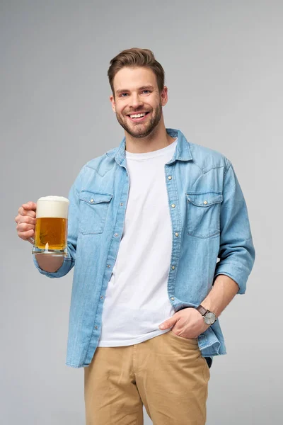 Young Man holding wearing jeans shirt holding glass of beer standing over Grey Background — Stock Photo, Image