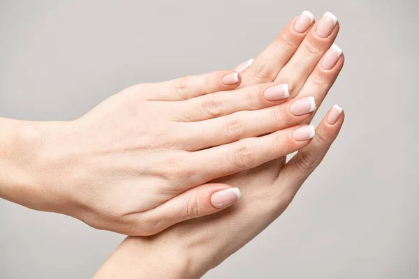 Mãos femininas bonitas com manicure francês sobre fundo cinza claro — Fotografia de Stock