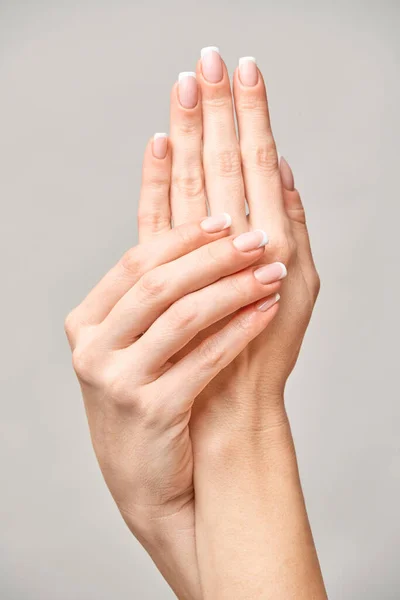 Mãos femininas bonitas com manicure francês sobre fundo cinza claro — Fotografia de Stock