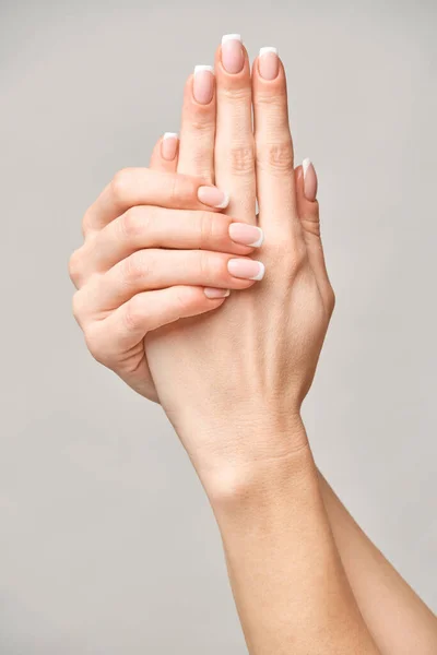 Mãos femininas bonitas com manicure francês sobre fundo cinza claro — Fotografia de Stock