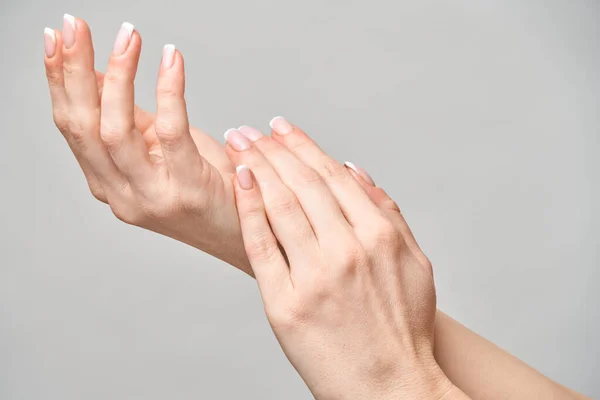 Mãos femininas bonitas com manicure francês sobre fundo cinza claro — Fotografia de Stock