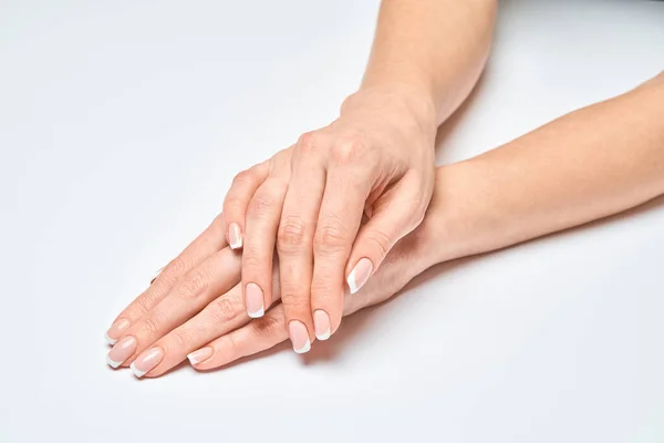 Piękne kobiece ręce z francuskim manicure na jasnoszarym tle — Zdjęcie stockowe