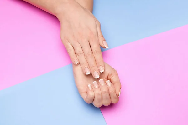 Mãos femininas bonitas com manicure francês sobre fundo de papel colorido — Fotografia de Stock