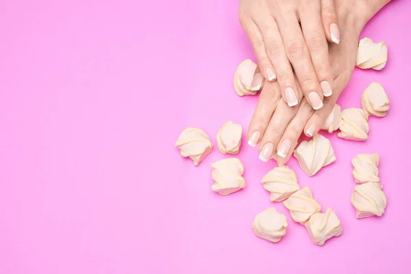 Beautiful Female Hands with French manicure and marshmallows over colorful pink paper background — Stock Photo, Image