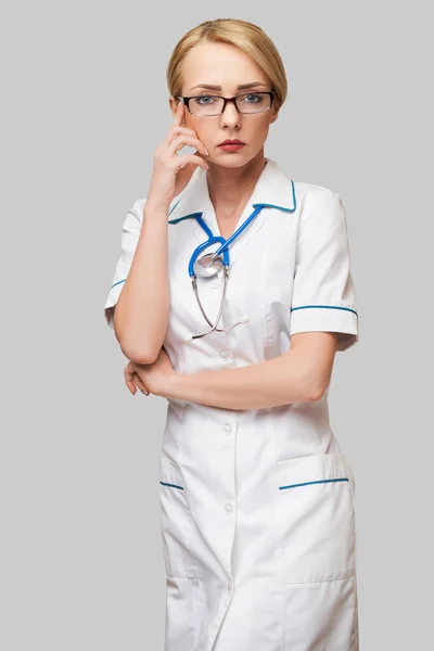 Retrato de una atractiva enfermera doctora joven en bata blanca sobre fondo gris claro — Foto de Stock