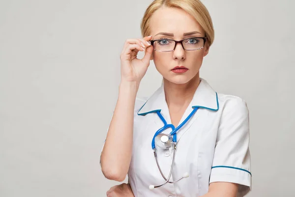 Retrato de una atractiva enfermera doctora joven en bata blanca sobre fondo gris claro —  Fotos de Stock