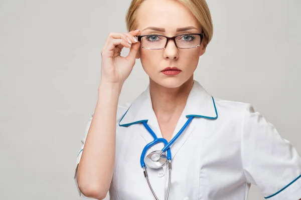 Retrato de una atractiva enfermera doctora joven en bata blanca sobre fondo gris claro —  Fotos de Stock