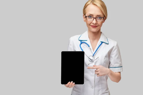 회색 배경에 분리 된 태블릿 패드를 들고 있는 아름다운 여성 의사 — 스톡 사진