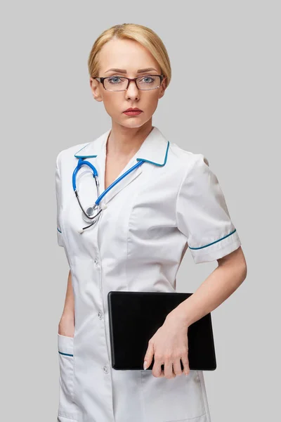 회색 배경에 분리 된 태블릿 패드를 들고 있는 아름다운 여성 의사 — 스톡 사진