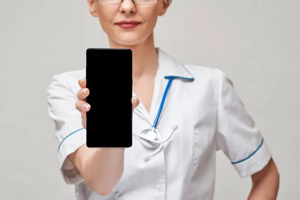 Kadın doktor ya da hemşire portresi boş ekranla cep telefonunu tutuyor ve gösteriyor — Stok fotoğraf
