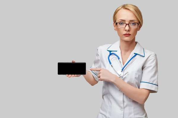 Retrato de una doctora o enfermera sosteniendo y mostrando teléfono móvil con pantalla en blanco —  Fotos de Stock