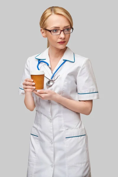 Porträtt av en kvinnlig läkare som håller papperskopp kaffe stående över grå bakgrund — Stockfoto
