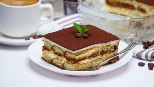 Tradycyjny włoski deser Tiramisu w szklanym naczyniu do pieczenia, porcja na talerzu i filiżanka kawy — Wideo stockowe