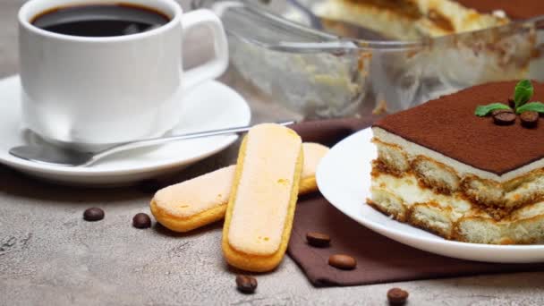 Postre Tiramisú tradicional italiano en bandeja para hornear de vidrio y porción sobre fondo de hormigón gris — Vídeo de stock