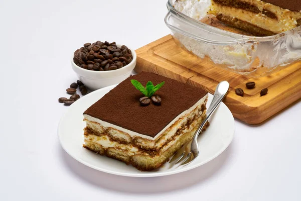 Tradicional postre Tiramisú italiano en plato de vidrio para hornear y porción en plato sobre fondo blanco — Foto de Stock