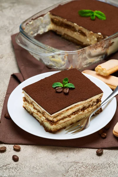 Традиционный итальянский десерт Тирамису в стеклянной выпечке, печенье Savoiardi и порция на сером бетонном фоне — стоковое фото