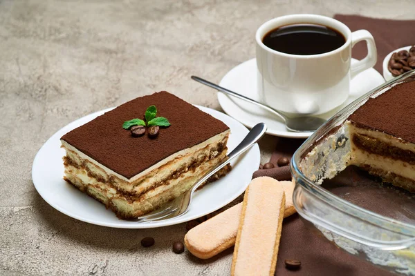 Tradycyjny włoski deser Tiramisu w szklanym naczyniu do pieczenia i porcja na szarym tle betonu — Zdjęcie stockowe