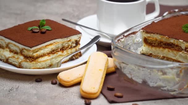 Traditioneel Italiaans Tiramisu dessert in glazen bakvorm en portie op grijze betonnen ondergrond — Stockvideo