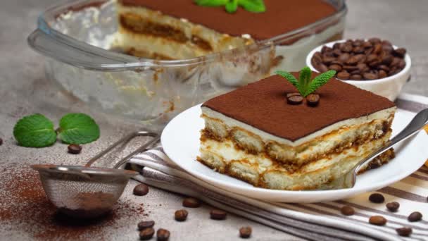 Traditional Italian Tiramisu dessert in glass baking dish and portion on grey concrete background — Stock Video