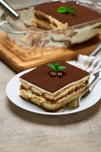 Традиционный итальянский десерт Tiramisu в стеклянной выпечке и порция на сером бетонном фоне — стоковое фото