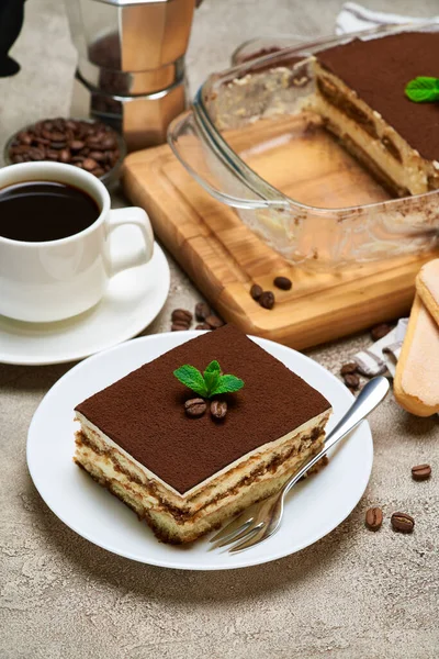 Traditionelles italienisches Tiramisu-Dessert in Glasauflaufform und Portion auf grauem Betongrund — Stockfoto