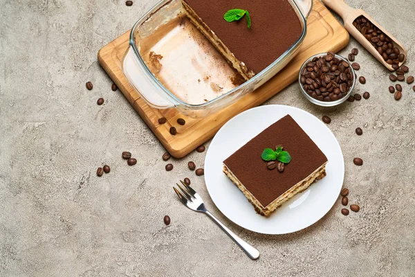 Traditionelles italienisches Tiramisu-Dessert in Glasauflaufform und Portion auf grauem Betongrund — Stockfoto