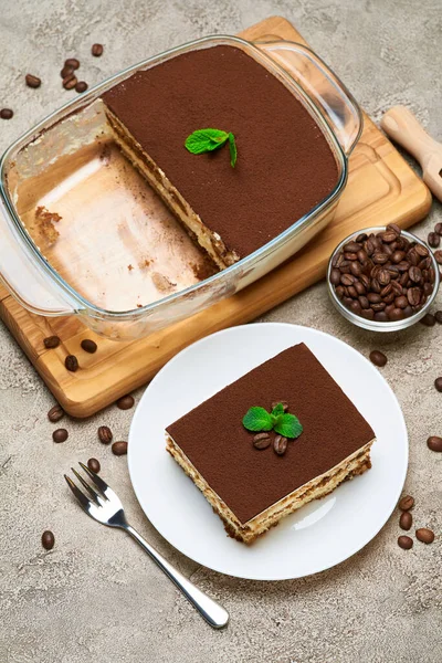 Postre Tiramisú tradicional italiano en bandeja para hornear de vidrio y porción sobre fondo de hormigón gris —  Fotos de Stock