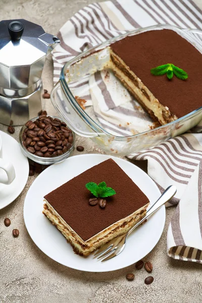 Postre Tiramisú tradicional italiano en bandeja para hornear de vidrio y porción sobre fondo de hormigón gris —  Fotos de Stock