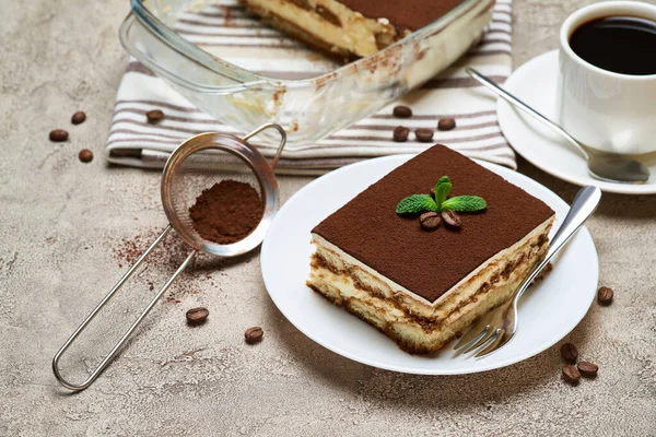Traditionelles italienisches Tiramisu-Dessert in Glasauflaufform und Portion auf grauem Betongrund — Stockfoto