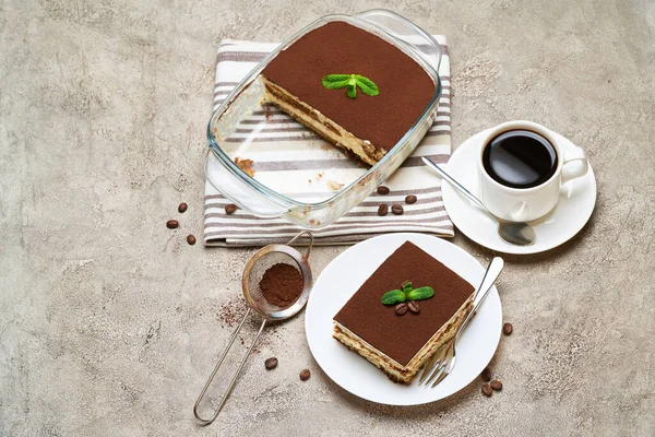 Traditionelles italienisches Tiramisu-Dessert in Glasauflaufform und Portion auf grauem Betongrund — Stockfoto