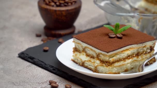 Traditional Italian Tiramisu dessert in glass baking dish and portion on grey concrete background — Stock Video